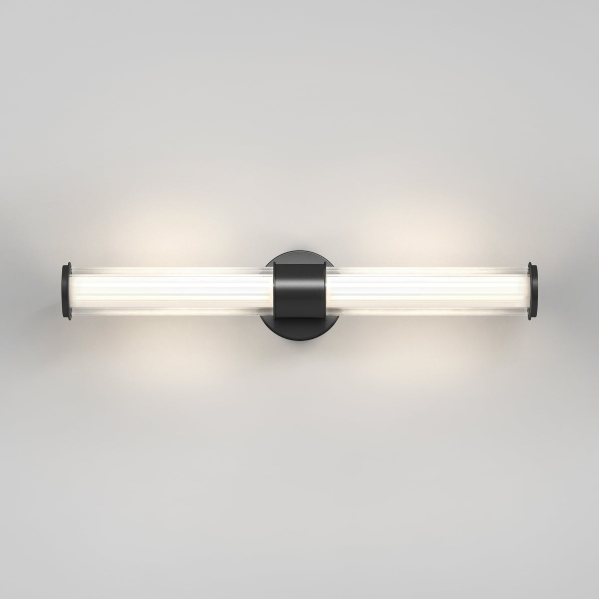 A modern wall-mounted light fixture with a cylindrical frosted glass tube and a black circular base, emitting a soft, diffused glow against a plain light gray wall.