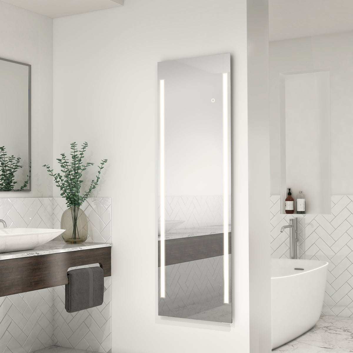 A modern bathroom with a wall-mounted rectangular LED mirror, a white freestanding bathtub, a wooden vanity with a vessel sink, a towel, two vases with greenery, and herringbone-patterned tile walls.
