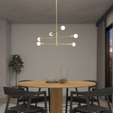 A modern dining room with a round wooden table, four dark chairs, a brass chandelier with exposed bulbs, a potted plant in the corner, and floor-to-ceiling windows with city views at dusk.