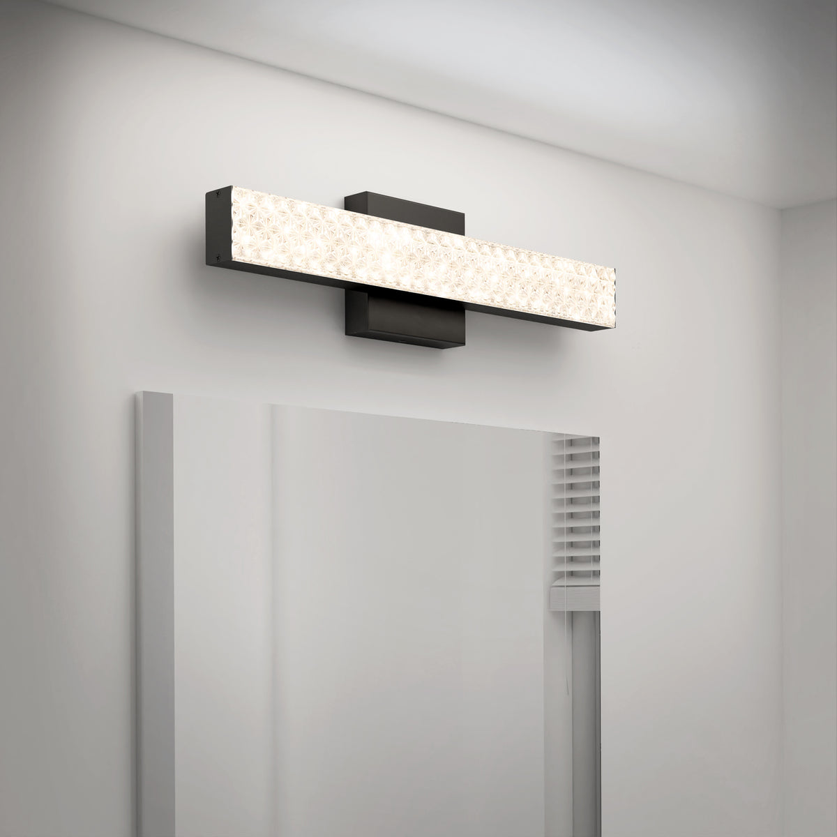 A modern rectangular wall sconce with a textured, illuminated front panel is mounted above a mirror on a white wall in a contemporary bathroom.