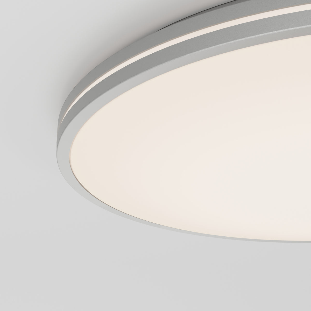 Close-up of a modern, circular ceiling light fixture with a smooth, white diffused cover and a thin gray trim, mounted on a white ceiling.