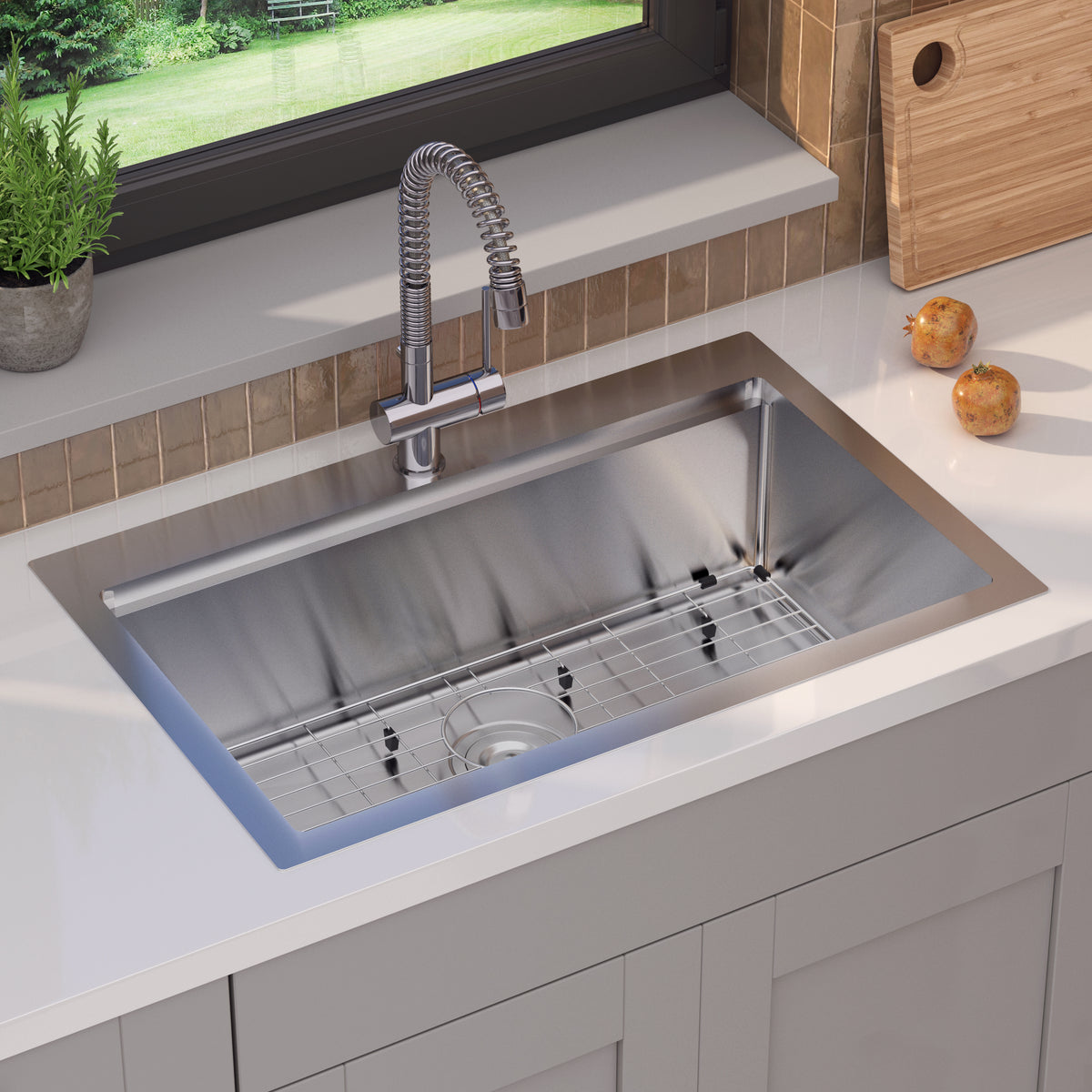 A modern stainless steel kitchen sink with a grid at the bottom, set in a white countertop. A flexible faucet is mounted above, and two potatoes and a cutting board are on the counter nearby, next to a window.