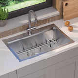 A modern stainless steel kitchen sink with a grid at the bottom, set in a white countertop. A flexible faucet is mounted above, and two potatoes and a cutting board are on the counter nearby, next to a window.