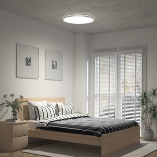 Modern bedroom with a wooden bed, striped bedding, framed art, potted plants, and the Artika Jupiter 23 in. LED flush mount light.