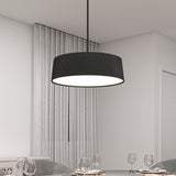 A modern black pendant light with a pleated shade hangs above a dining table set with wine glasses, in a minimalist room with white walls, light gray curtains, and simple decor.