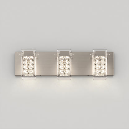 A modern wall-mounted light fixture with three rectangular, crystal-accented lights on a brushed metal base, emitting a bright, even glow against a plain light gray background.