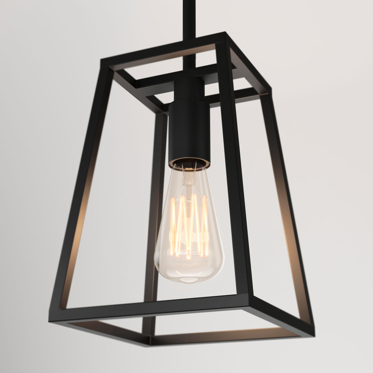 A modern pendant light with a black, geometric metal frame and an exposed glowing filament bulb hanging against a plain white background.