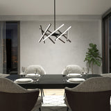 A modern dining room with a black table set for four, cushioned gray chairs, a geometric chandelier, a potted plant, large windows, and neutral-colored walls.