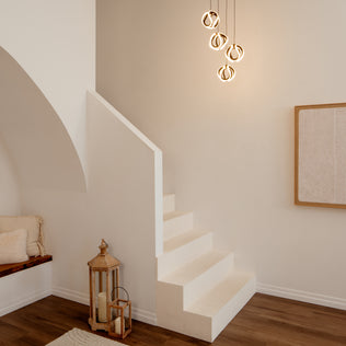 A minimal, modern stairway in a neutral room with white walls, wood floors, abstract wall art, decorative lanterns by the stairs, and an Artika Vivaldi modern LED 4-light pendant illuminating the space.