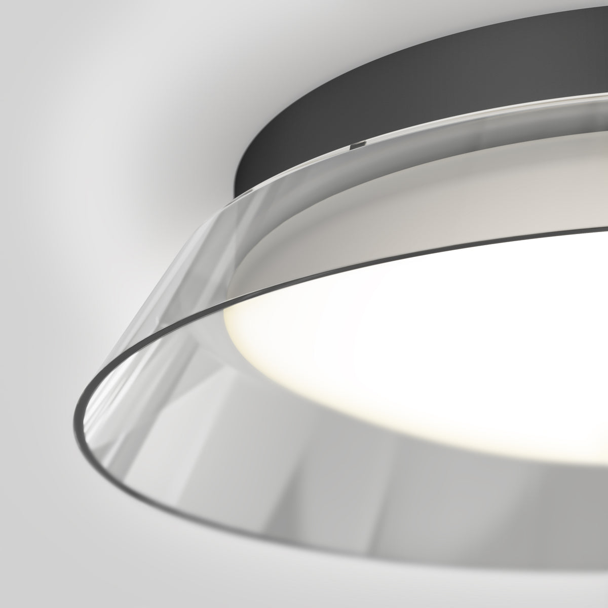 Close-up view of a modern ceiling light fixture with a black base and a transparent, circular acrylic or glass shade, emitting a soft, diffused white light against a neutral background.