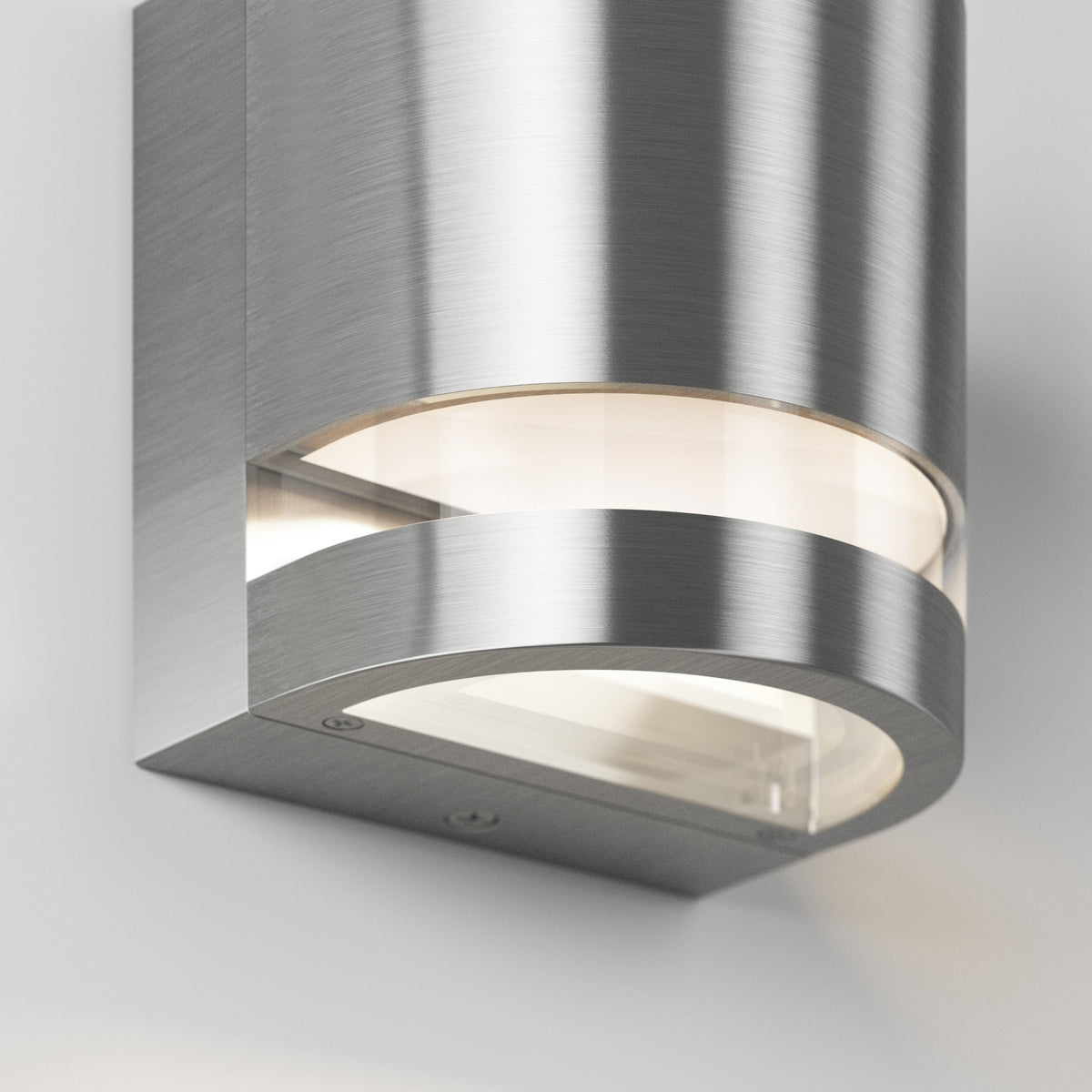 A close-up of a modern wall-mounted light fixture with a brushed metal finish and curved design, emitting soft light from behind a frosted glass panel.