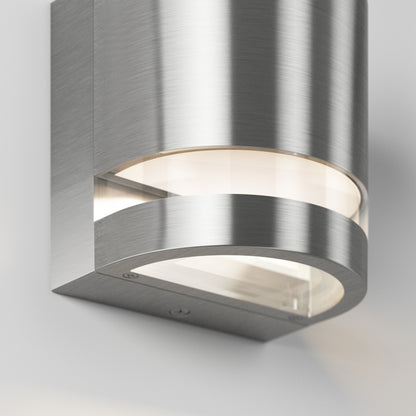 A close-up of the Artika Valor Round LED indoor-outdoor wall light features a modern, curved brushed metal design, mounted on a white wall and emitting light from both the top and bottom edges.