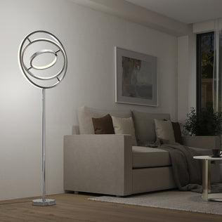 A modern living room featuring a beige sofa, brown and cream cushions, a dark throw, and the Artika Pivot modern LED floor lamp (3 CCT) with circular rings, set beside a coffee table and wall art.