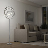 A modern living room with a beige sofa, brown and cream cushions, a gray throw blanket, abstract wall art, and a unique circular LED floor lamp beside the sofa. A small round coffee table sits in front.