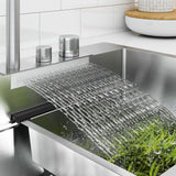 Water flows in a wide, flat stream from a modern kitchen faucet into a stainless steel sink, rinsing fresh green beans. The kitchen background is clean and contemporary.