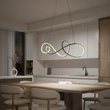Modern kitchen and dining area with light wooden furniture, beige chairs, and a sculptural, looped LED pendant light hanging above the table. Minimalist decor with neutral tones and soft lighting.
