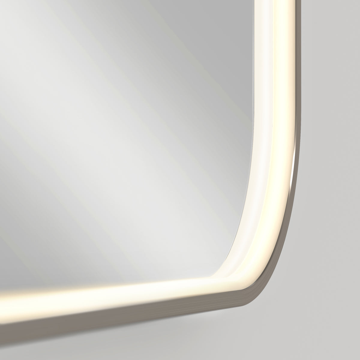 Close-up of the Royce Dimmable LED Mirror by Artika, featuring rounded edges and adjustable 3 CCT LED lighting along its border, emitting a soft, even glow on a light gray wall. Can be mounted horizontally or vertically.