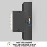 A black rectangular wall switch with a colour temperature control dial is mounted vertically on a light grey wall. A label indicates Colour Temperature Switch in English, French, and Spanish.