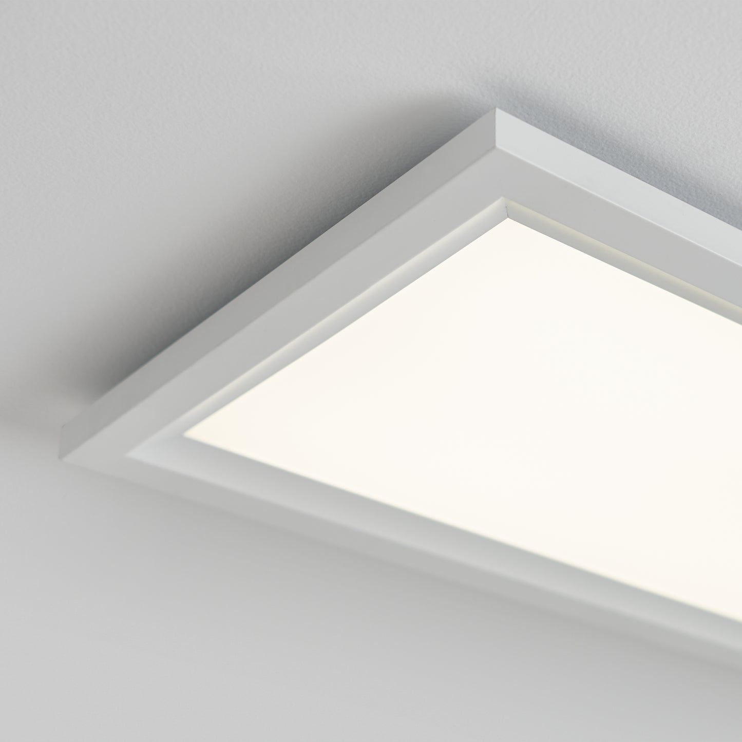 A close-up of the Artika Sunray ultra thin LED light panel 3 CCT, a rectangular modern fixture with a white frame, mounted on a white ceiling and emitting bright light.