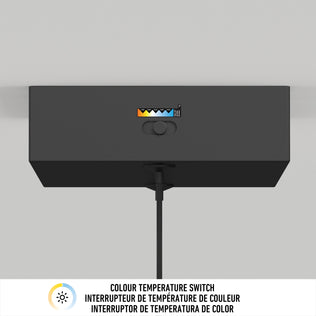 The Artika Coda modern LED pendant light 5 CCT is a black rectangular fixture with a color temperature switch and indicator for various settings, mounted on the wall. A cable hangs below. COLOUR TEMPERATURE SWITCH appears in three languages underneath.