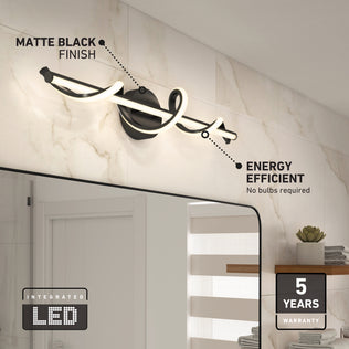 The Artika Coda 27-in Integrated LED 5-CCT Vanity Light Bar, shown in matte black above a bathroom mirror, offers energy efficiency, an integrated LED, and a 5-year warranty. Shelves with towels and décor appear in the background.