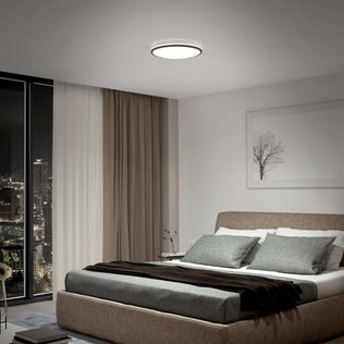 Modern bedroom with a large bed, gray bedding, city view window, and an Artika Macy 15 in. RGB Wifi LED flush mount light overhead.