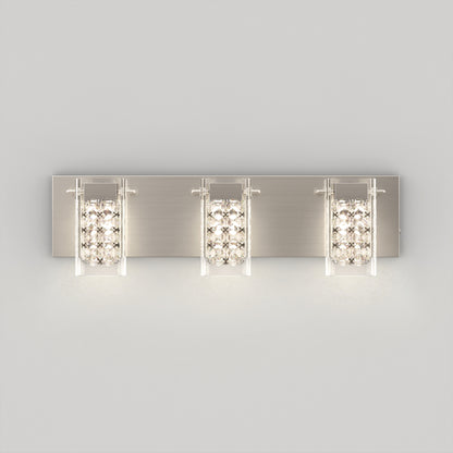 A modern three-light wall sconce with a brushed metal rectangular base, each light featuring a clear glass shade and a row of decorative crystal-like accents, mounted on a plain light gray wall.