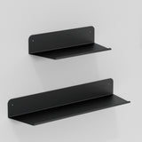 Two black metal floating shelves are mounted on a plain white wall, one above the other, with the upper shelf being smaller than the lower one. Both shelves have a minimalist, modern design.
