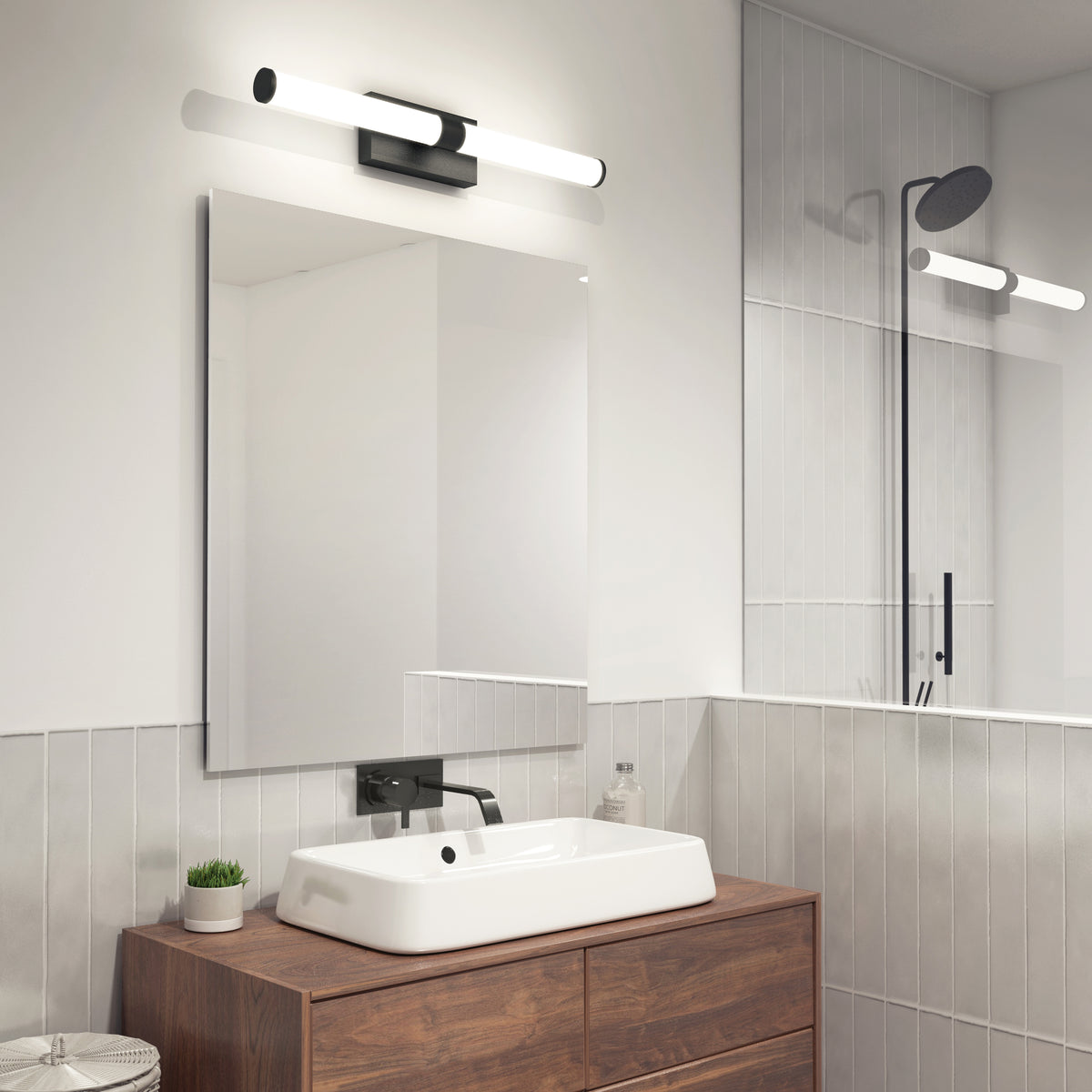 Modern bathroom with a rectangular mirror, white rectangular sink on a wooden vanity, wall-mounted faucet, potted plant, soap dispenser, and a glass shower enclosure with a black showerhead and light fixture.