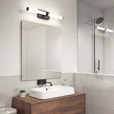 Modern bathroom with a rectangular mirror, white rectangular sink on a wooden vanity, wall-mounted faucet, potted plant, soap dispenser, and a glass shower enclosure with a black showerhead and light fixture.