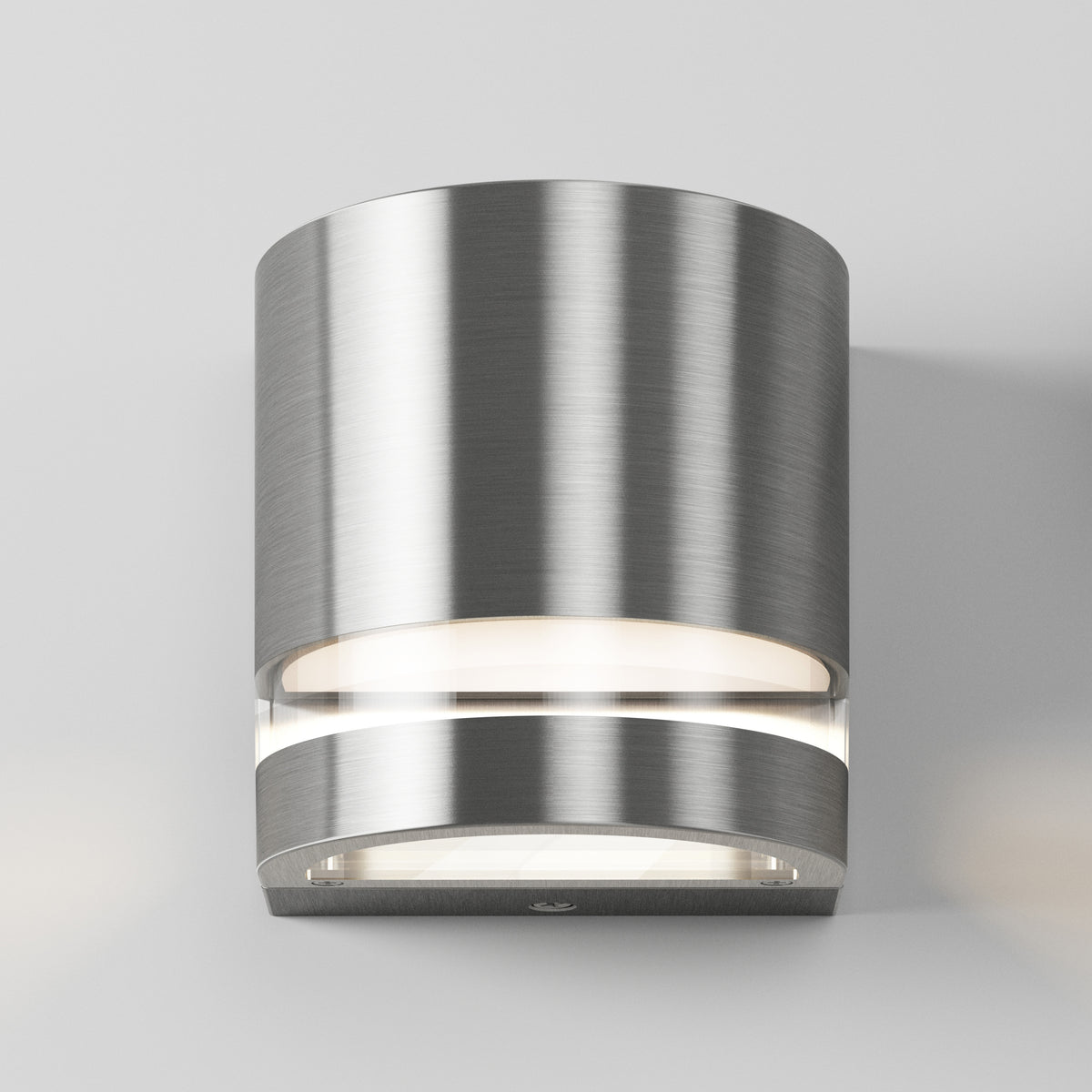 A modern wall-mounted light fixture with a brushed metal cylindrical body emits soft white light from both the top and bottom, set against a plain light gray background.