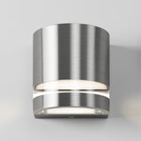 A modern wall-mounted light fixture with a brushed metal cylindrical body emits soft white light from both the top and bottom, set against a plain light gray background.
