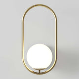 A modern wall sconce featuring a round white globe light set within an elongated oval gold metal frame against a light gray background.