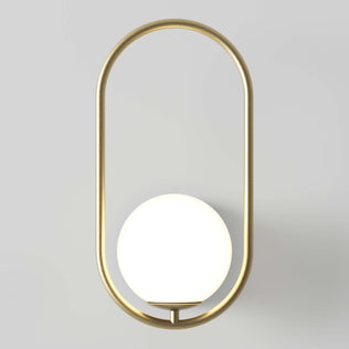 The Artika Bloom LED Sconce 3 CCT showcases a round white globe light set inside a vertical, oval gold metal frame, creating a modern accent against any light gray wall.