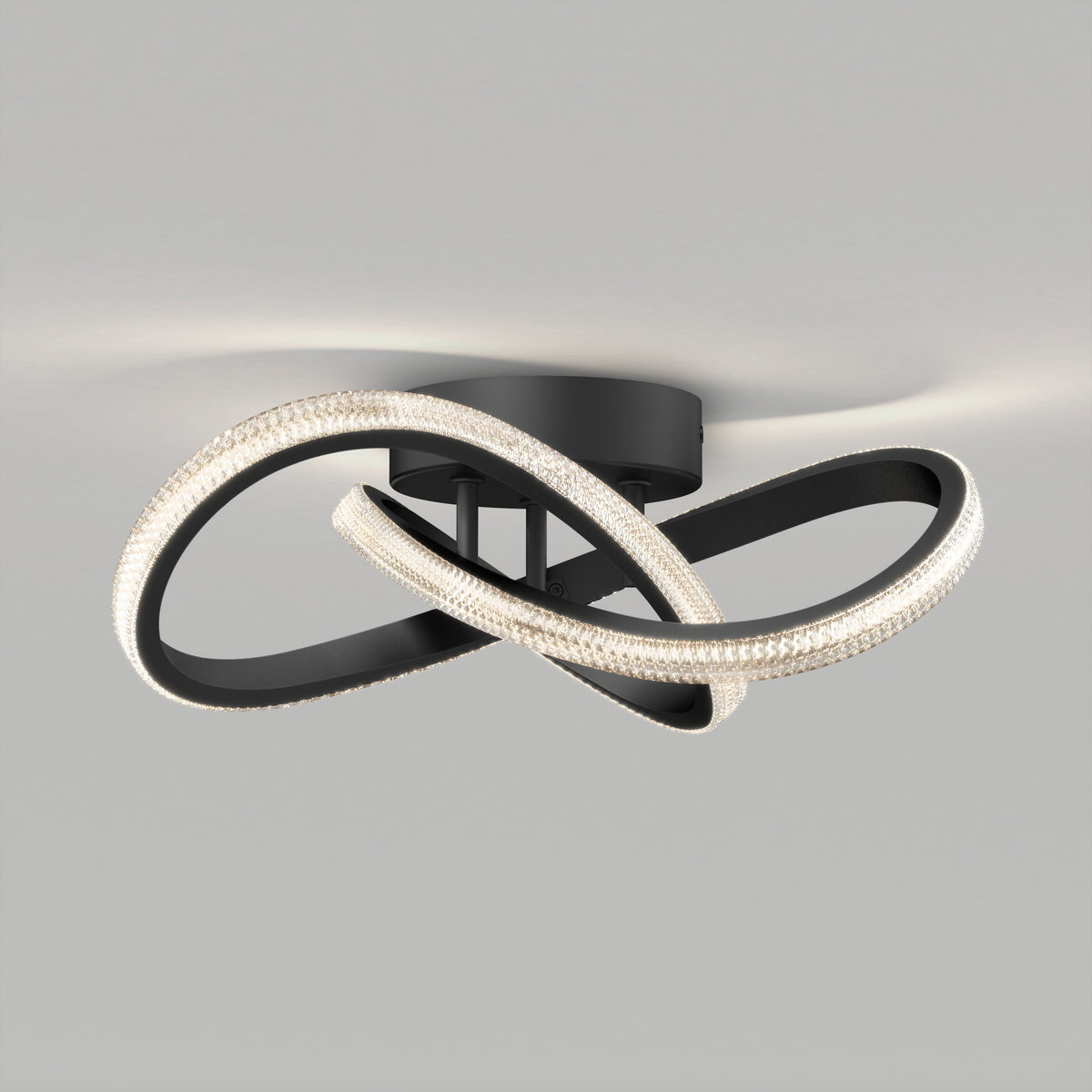 Ceiling light fixture with two intertwined, looped LED bands attached to a round black base, emitting a soft, even glow against a plain gray ceiling.