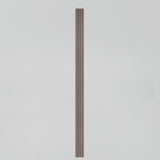 A tall, narrow, vertical object with parallel grooves, resembling a fluted column, stands centered against a plain light gray background.