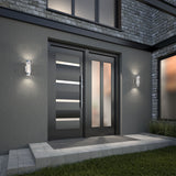 Modern front entrance with a sleek black double door featuring horizontal glass panels, frosted side window, two wall-mounted lights, stone steps, and a combination of smooth and brick exterior walls.