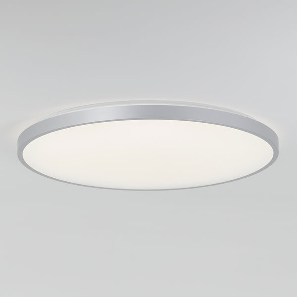 The Artika Jupiter 23 in. LED flush mount light features a modern round design with a white diffused cover and silver rim, mounted on a plain white ceiling. Includes remote control.