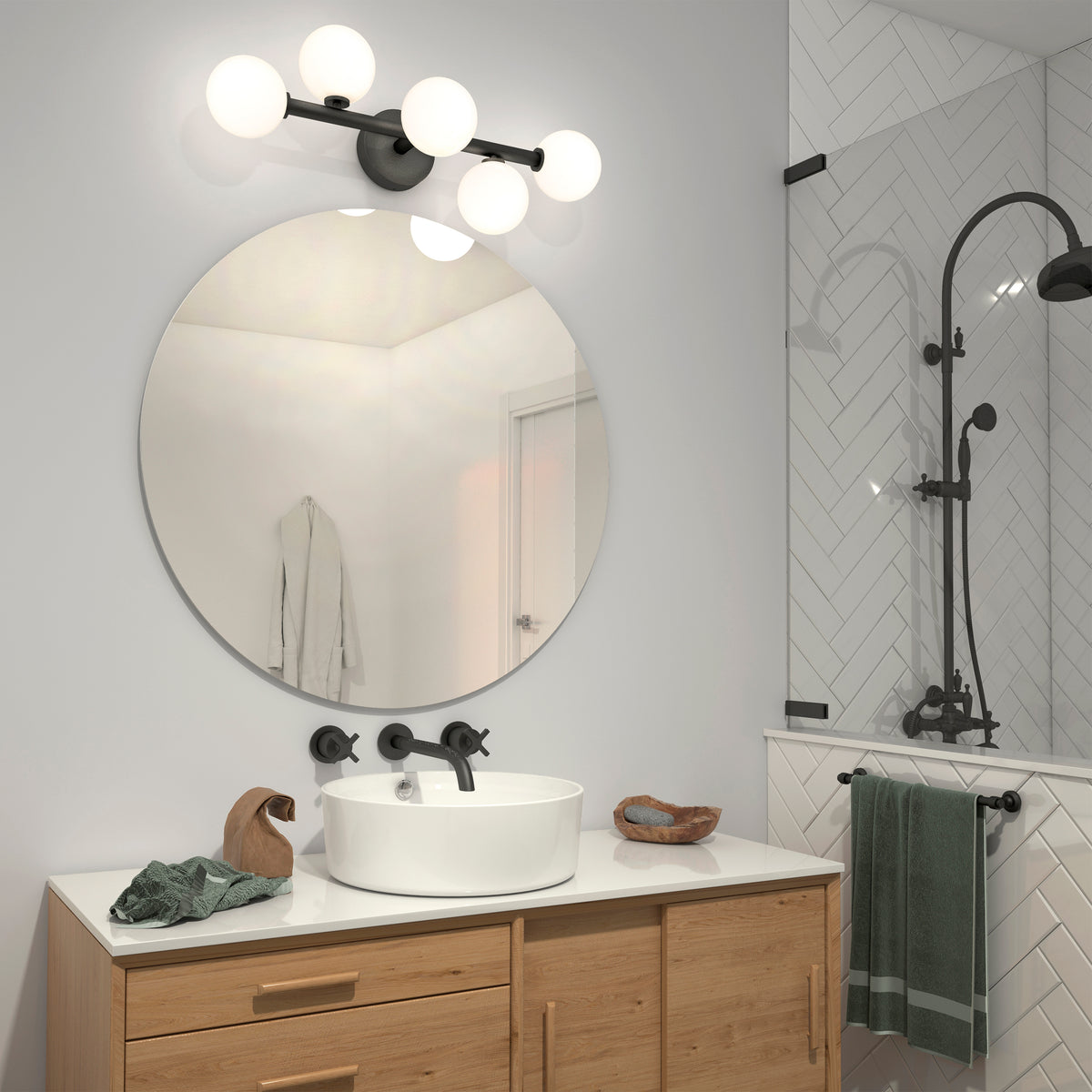 Modern bathroom with a round mirror above a wooden vanity, vessel sink, and black fixtures. The Artika Bloom 27-in 3-Light Modern LED Vanity Light brightens the space, while towels hang beside a glass shower with herringbone tile and black showerhead.