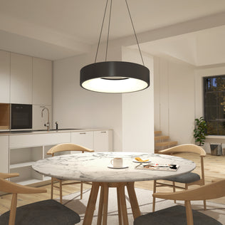 A modern kitchen and dining area features a marble round table, four wooden chairs, and the Artika Aiden LED pendant light hanging above. White cabinets line the kitchen, with stairs visible in the background.