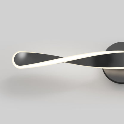 The Artika Finley LED modern bathroom vanity light 3 CCT features a minimalist, twisted ribbon design in black and white, mounted on a round black base against a plain light gray background.