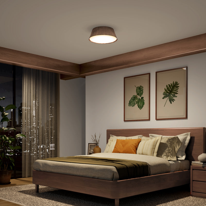 Modern bedroom with a walnut bed, green/beige bedding, plant art, skyline views, and an Artika Dunham 15 in. LED flush mount light.
