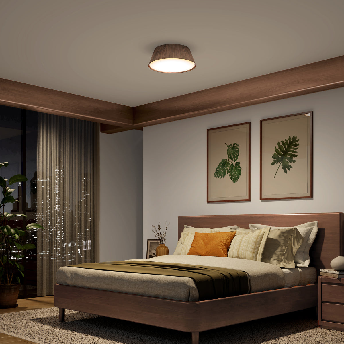 A cozy modern bedroom with a wooden bed, earth-toned bedding, two botanical prints on the wall, a round ceiling light, and a night view of a city skyline visible through large windows with sheer curtains.
