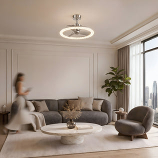 Modern living room with a gray sofa, round coffee table, Artika Carat 23" LED Ceiling Fan, large window, and blurred woman walking.
