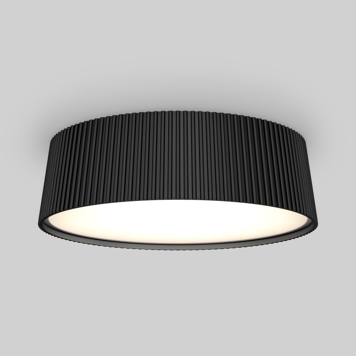 A modern ceiling light fixture with a wide, cylindrical black shade featuring vertical grooves, emitting a soft, even glow against a plain gray background.