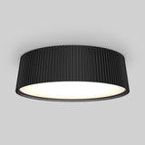 A modern ceiling light fixture with a wide, cylindrical black shade featuring vertical grooves, emitting a soft, even glow against a plain gray background.