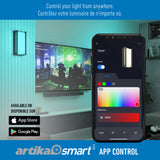 A smart wall light is shown in a modern living room above a TV. A smartphone displays the Artika Smart app, allowing color and brightness control. App Store and Google Play logos are visible. Text is in English and French.