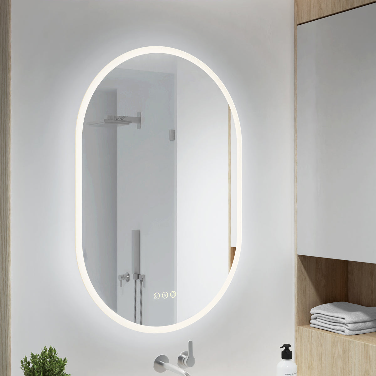 Artika’s Clara LED Mirror Oval 30x20″ with Defogger reflects a shower; shelves nearby hold towels and a soap dispenser.