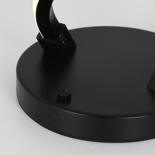 Close-up of the Artika Swirl LED table lamp’s modern black round base with a small button, showing part of its arching dimmable LED design on a light surface.