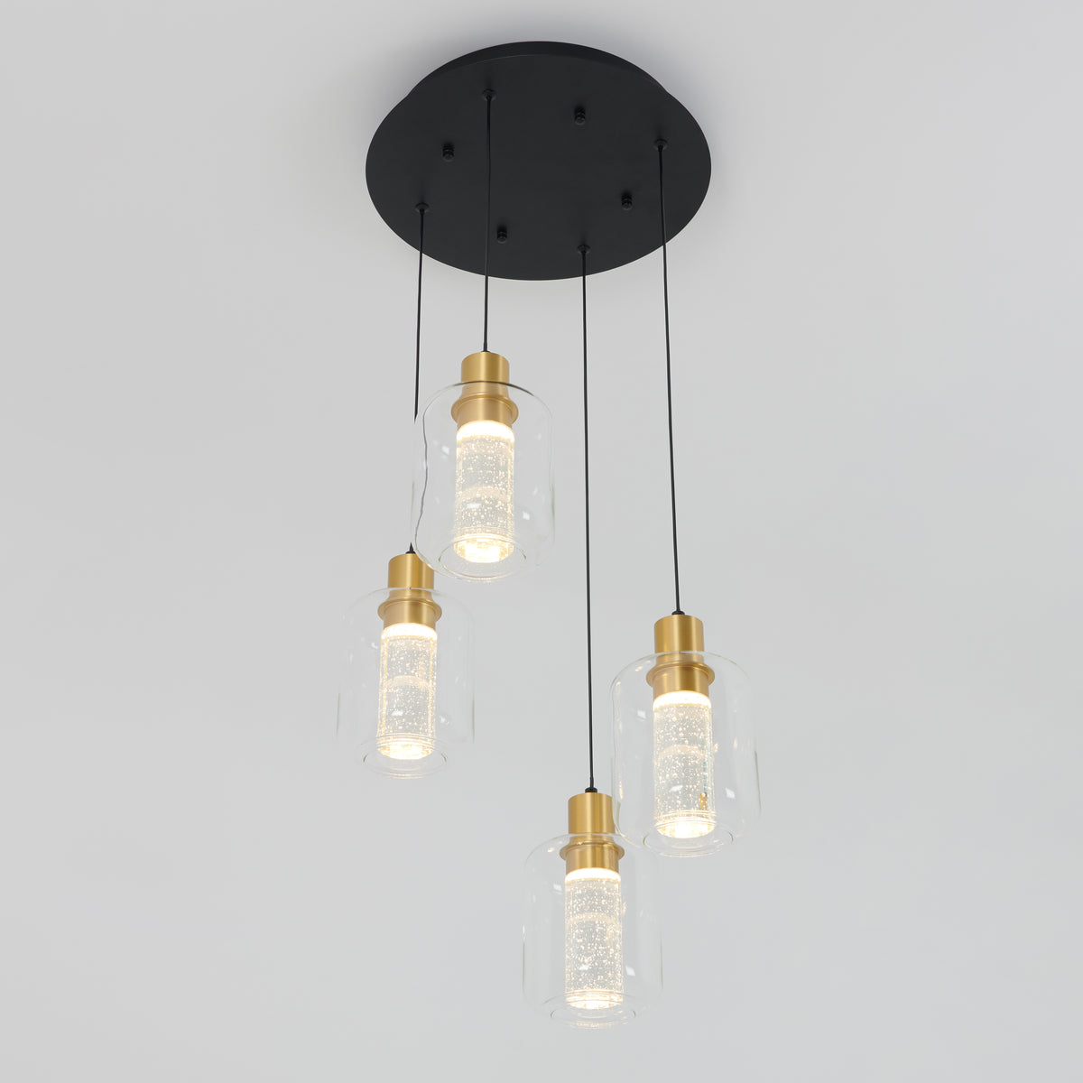 A modern ceiling light fixture with four hanging pendant lights, each featuring a cylindrical glass shade, gold accents, and a black circular base against a plain white background.